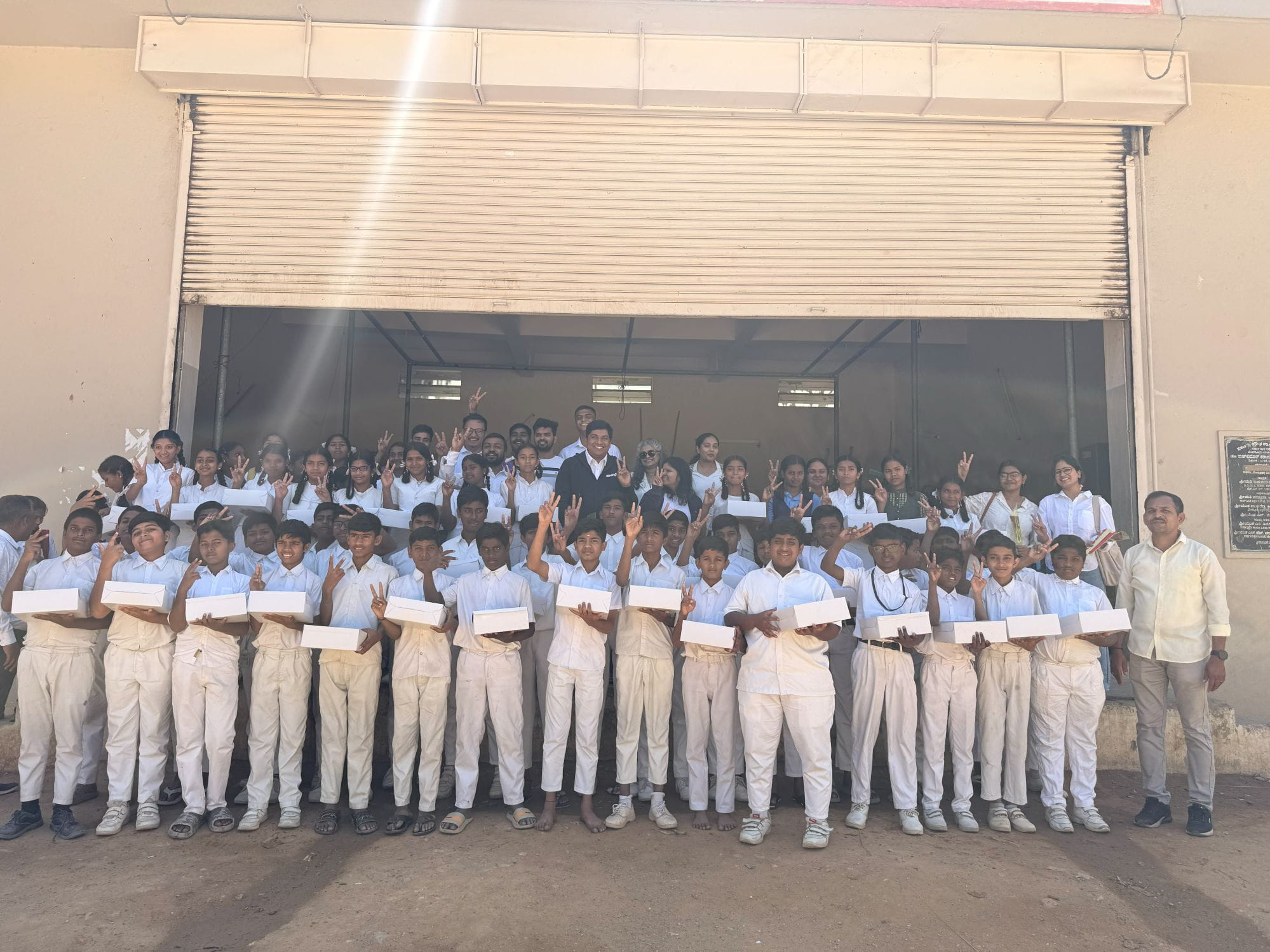 Group photo of students and volunteers holding donated laptops during the 2026 Bangalore laptop donation drive.