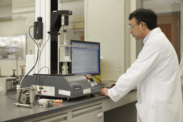 Laboratory technician operating a materials testing machine for combination product verification and performance testing.
